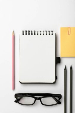 Ofis malzemeleri, defter, kalemler ve yapışkan notlarla dolu beyaz bir masanın yakın çekimi.