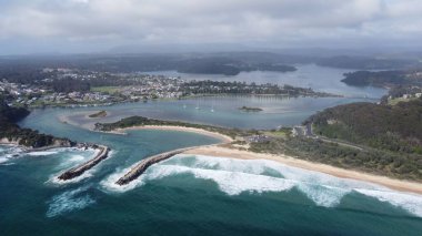 Wagonga Head 'in arka planda tepeler ve ormanlar ile bulutlu bir gökyüzünün altında çekilmiş bir fotoğrafı.