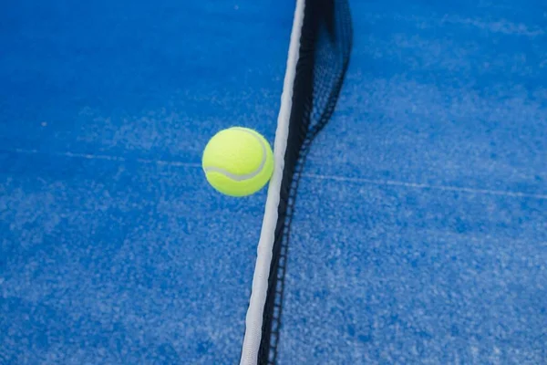 a ball in the air over the net of a paddle tennis court