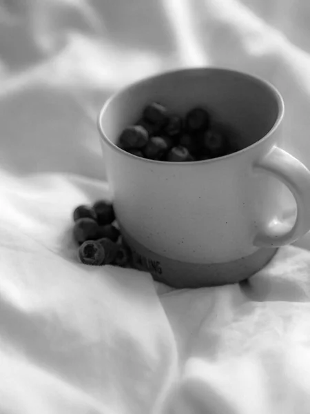 Eine Vertikale Graustufenaufnahme Einer Mit Blaubeeren Gefüllten Tasse Auf Bettlaken — Stockfoto