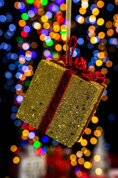 背景には 金色に包まれたクリスマスプレゼントの縦に赤のリボンとボケのライトが描かれています — ストック写真