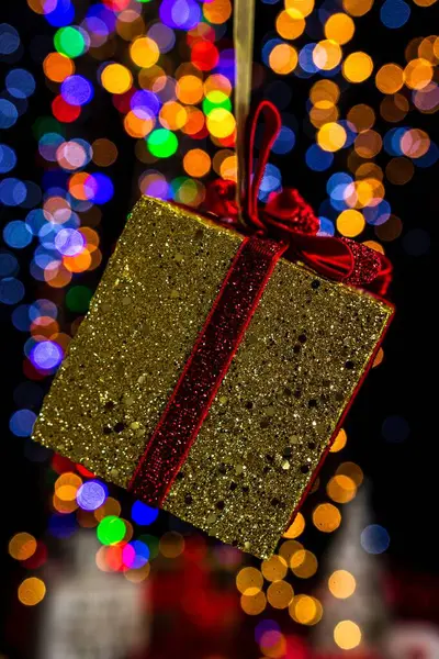 背景には 金色に包まれたクリスマスプレゼントの縦に赤のリボンとボケのライトが描かれています — ストック写真