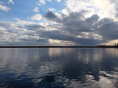Deniz ve Yunanistan 'ın Kalamata limanı üzerindeki mavi gökyüzündeki bulutlar arasındaki güneş ışınlarının manzarası