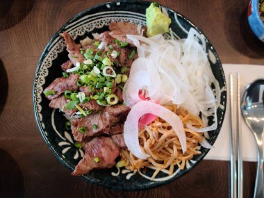 Masadaki kasede pişmiş et, doğranmış soğan ve diğer sebzelerden oluşan bir manzara.