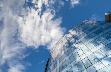 Gökdelenin yukarı yakın görüntüsü mavi gökyüzündeki bulutları yansıtıyor.