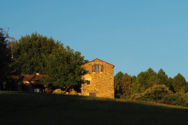 Dordogne, Fransa 'da açık mavi bir gökyüzünün altında yemyeşil ağaçlarla çevrili eski bir tuğla ev.