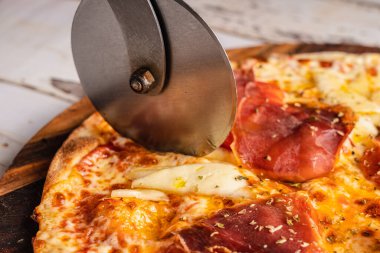 Metalik bir pizza dilimleyicisi İspanyol jambonlu pizzasını kesiyor..