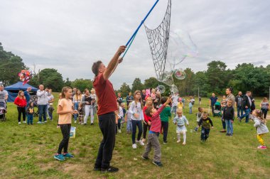 Polonya 'nın Malta Parkı' nda onları yakalamaya çalışan bir grup mutlu çocuk için büyük sabun köpükleri yaratan bir adam.