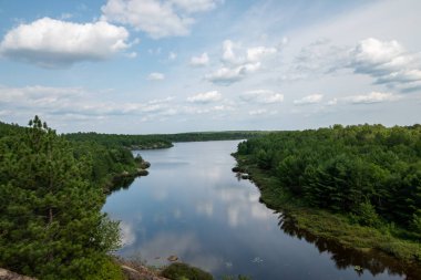Kanada 'daki güzel Laurentian Gölü güneşli bir günde mavi bulutlu bir gökyüzünün altında ağaçlarla çevrili.