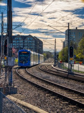 Stockholm 'de hafif bulutlu bir günde paralel raylardan yaklaşan mavi bir tramvayın yakın çekimi