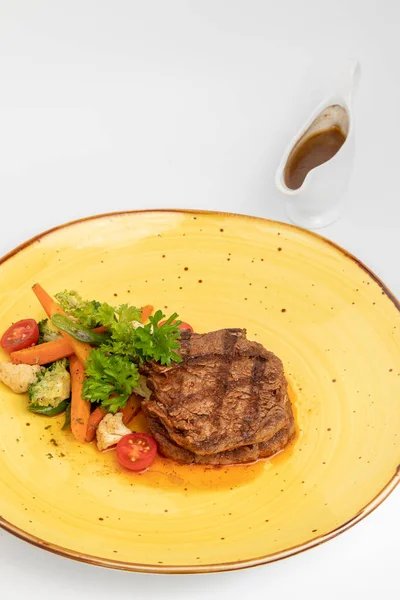 黄色の皿に盛り付けられた野菜のサイドディッシュと肉ステーキの垂直ショット — ストック写真