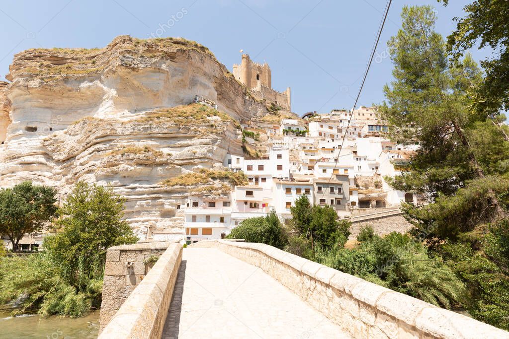 A view of the city of Alcala del Jucar with the buildings located on a hill against a cloudless sky