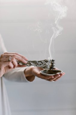 Adaçayı yakan ve deniz kabuğunun üzerinde tutan bir kadının dikey görüntüsü..