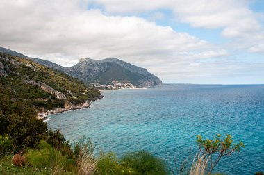 Bulutlu arka planda dağlarla çevrili bir deniz manzarası