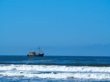 Açık mavi gökyüzünün altında güneşli bir günde Ameland, Hollanda 'da Wadden Denizi' nde yelken açan bir gemi.