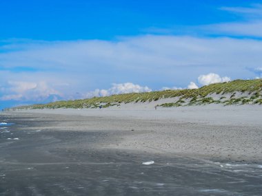 Hollanda, Ameland sahilinde çimlerle kaplı bir tepe Wadden Denizi kıyısında parlak mavi bir gökyüzünün altında