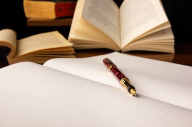 Açık bir defterin ve arka planda kitaplar olan eski bir kalemin sığ odağı