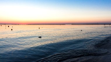 Güzel bir kıyı şeridi manzarası ve ufukta renkli bir gökyüzü olan büyük deniz suyu.