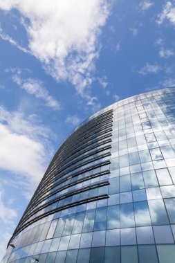 Gökdelenin yukarı yakın görüntüsü mavi gökyüzündeki bulutları yansıtıyor.