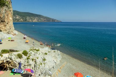 İtalya 'nın Centola kentinde Spiaggia della Marinella' da güneşli bir gökyüzünün altında güzel bir mavi su ve kayalık dağ manzarası.