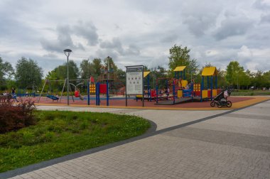 Polonya 'daki Rataje parkında çalıların ve renkli bir oyun parkının fotoğrafı.