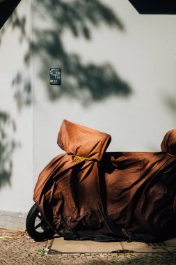 Duvarın yanına park etmiş kahverengi kumaşla kaplı bir motosiklet.