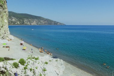 İtalya 'nın Centola kentinde Spiaggia della Marinella' da güneşli bir gökyüzünün altında güzel bir mavi su ve kayalık dağ manzarası.