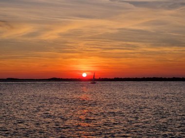 Gün batımında suda yüzen bir tekne silueti.