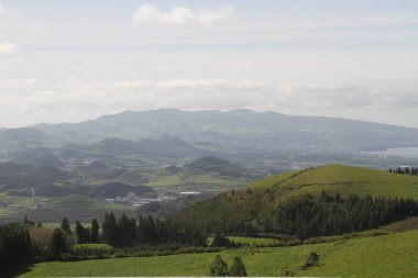 Bulutlu bir gökyüzünün altında yeşil bir tepe.