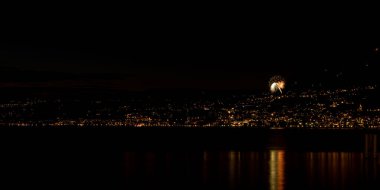 Gece ışıklarıyla şehrin yukarısındaki suya yansıyan havai fişeklerin uzun pozu