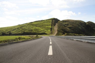 Bulutlu bir günde yeşil tepelere karşı boş bir asfalt yolun manzarası.