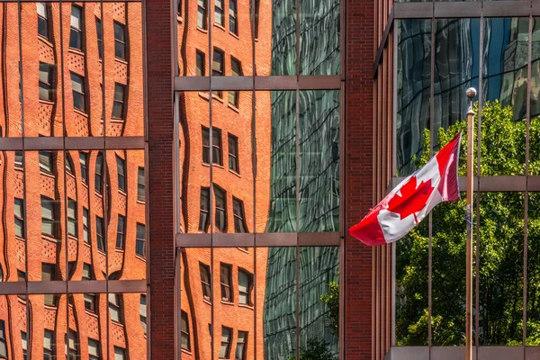 カナダの国旗を掲揚する極の横にある大きな窓のガラスの後ろのオレンジ色の建物の眺め — ストック写真