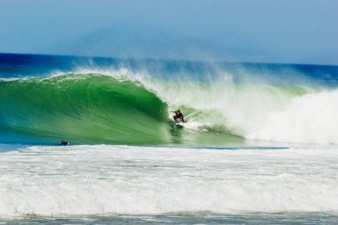 Turkuaz deniz dalgalarında sörf yapan bir erkek.