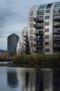 Mavi gökyüzü arka planındaki göle bakan modern apartmanların dikey görüntüsü.