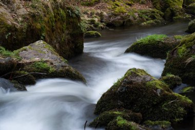 Etrafı yosunlu kayalarla çevrili sisli bir nehrin yakın çekim görüntüsü.