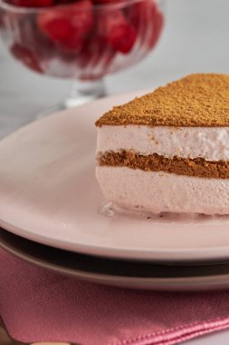 Üçlü çikolatalı kremalı pasta dilimi ve çilekli bir kase.