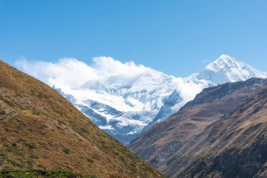 Mavi gökyüzünün altında karla kaplı tepeleri olan güzel bir dağ manzarası.