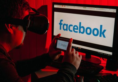 Facebook yeniden markalaşma kavramı. Elinde Meta logosu olan bir adam Facebook logosu olan bir bilgisayarın önünde oturuyor.