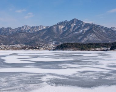 Donmuş gölün yanındaki yüksek kayalık bir dağın manzarası.