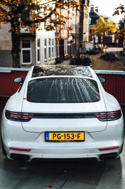 Arka planda ağaçlar ve binalar olan bir caddede park etmiş beyaz bir Porsche 'nin dikey görüntüsü.