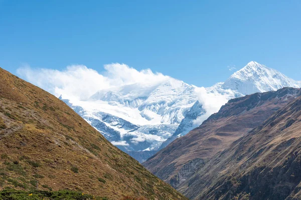 Mavi gökyüzünün altında karla kaplı tepeleri olan güzel bir dağ manzarası.
