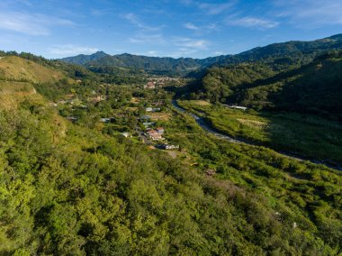 Kırsal bölgedeki tepelik arazide yeşilliklerle çevrili bir köyün hava görüntüsü.