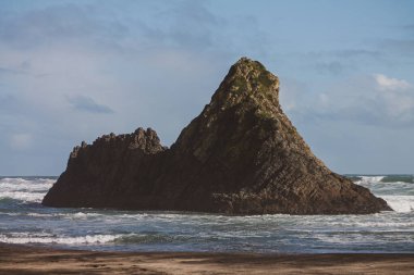 Yeni Zelanda 'da mavi bulutlu bir gökyüzünün altında Karekare Sahili' nde kayaların yakın çekimi.