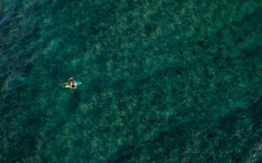 Sakin bir suda yüzen bir erkek sörfçünün havadan görünüşü.