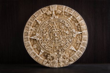 A round engraved stone with Aztec calendar on a wooden background clipart
