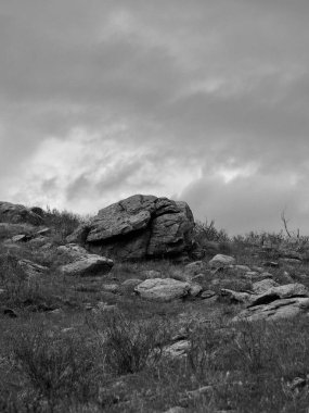 Kayalık bir dağdaki büyük kayaların gri tonda dikey görüntüsü..