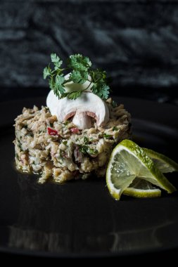 Lezzetli bir balık salatası, çeşitli sebzeler ve limonlu siyah bir tabakta.