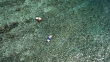 Sakin bir suda yüzen bir erkek sörfçünün havadan görünüşü.