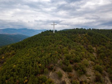 Ağaçlı yeşil bir manzara ve tepede bir haç.