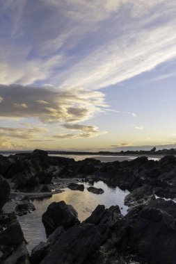 Gün batımında deniz kenarında büyük kayaların dikey görüntüsü.
